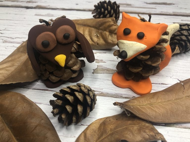 A pine cone and polymer clay fox and owl sitting amongst some autumnal leaves and pinecones