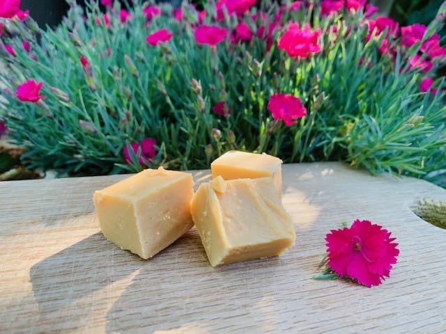 Pieces of traditional fudge sat on a wooden table with pink flowers in the background
