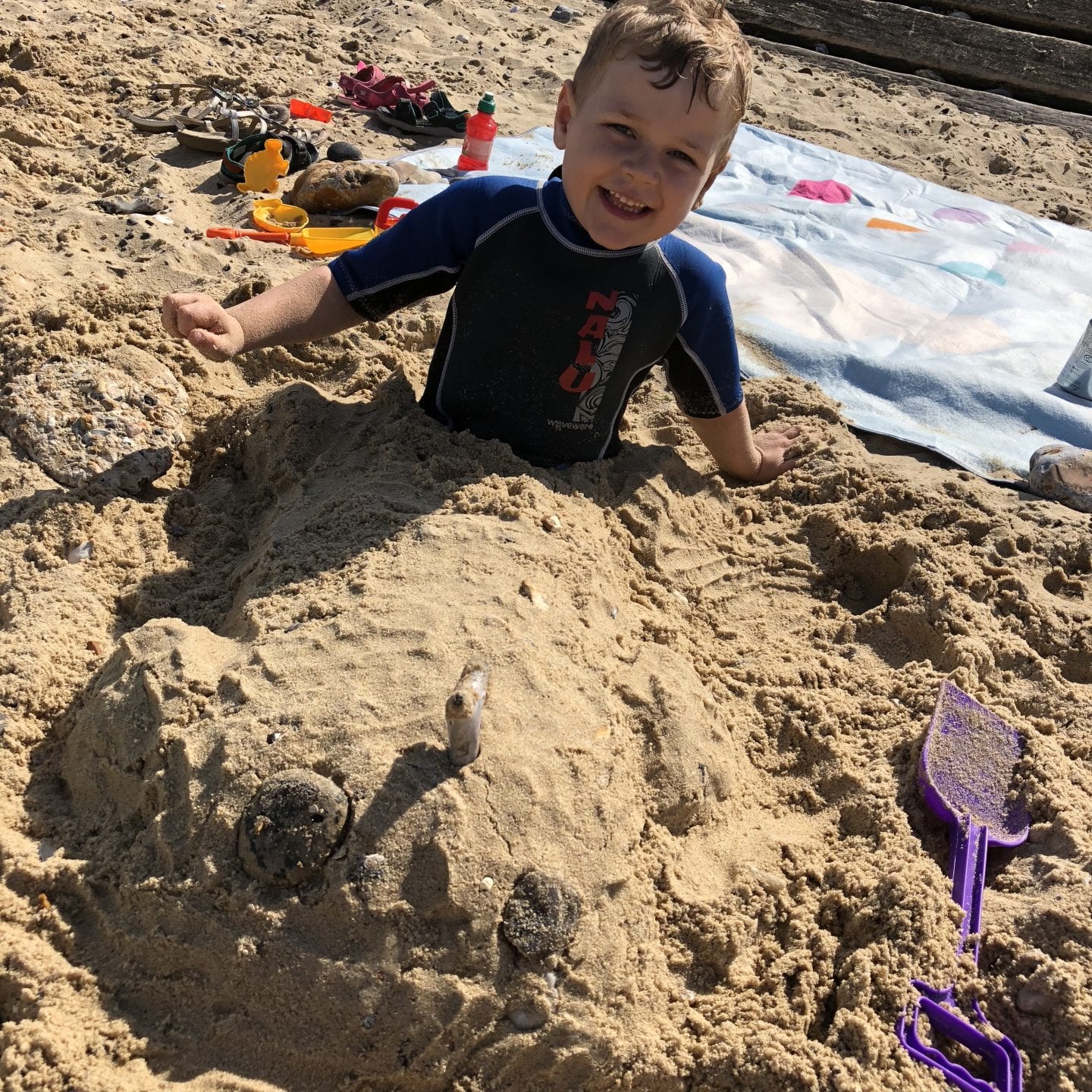 young boy with legs buried in the sand on a beach