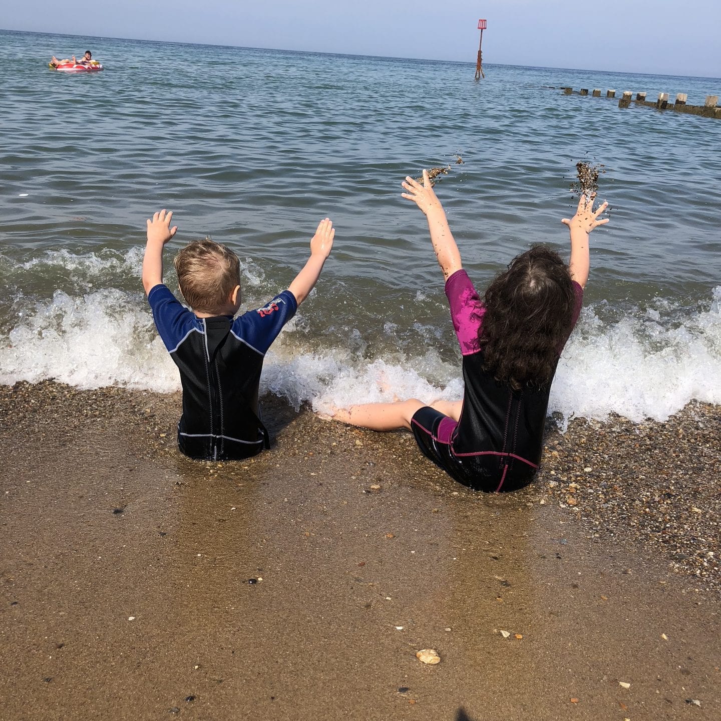 2 young children sitting on a beach in the surf