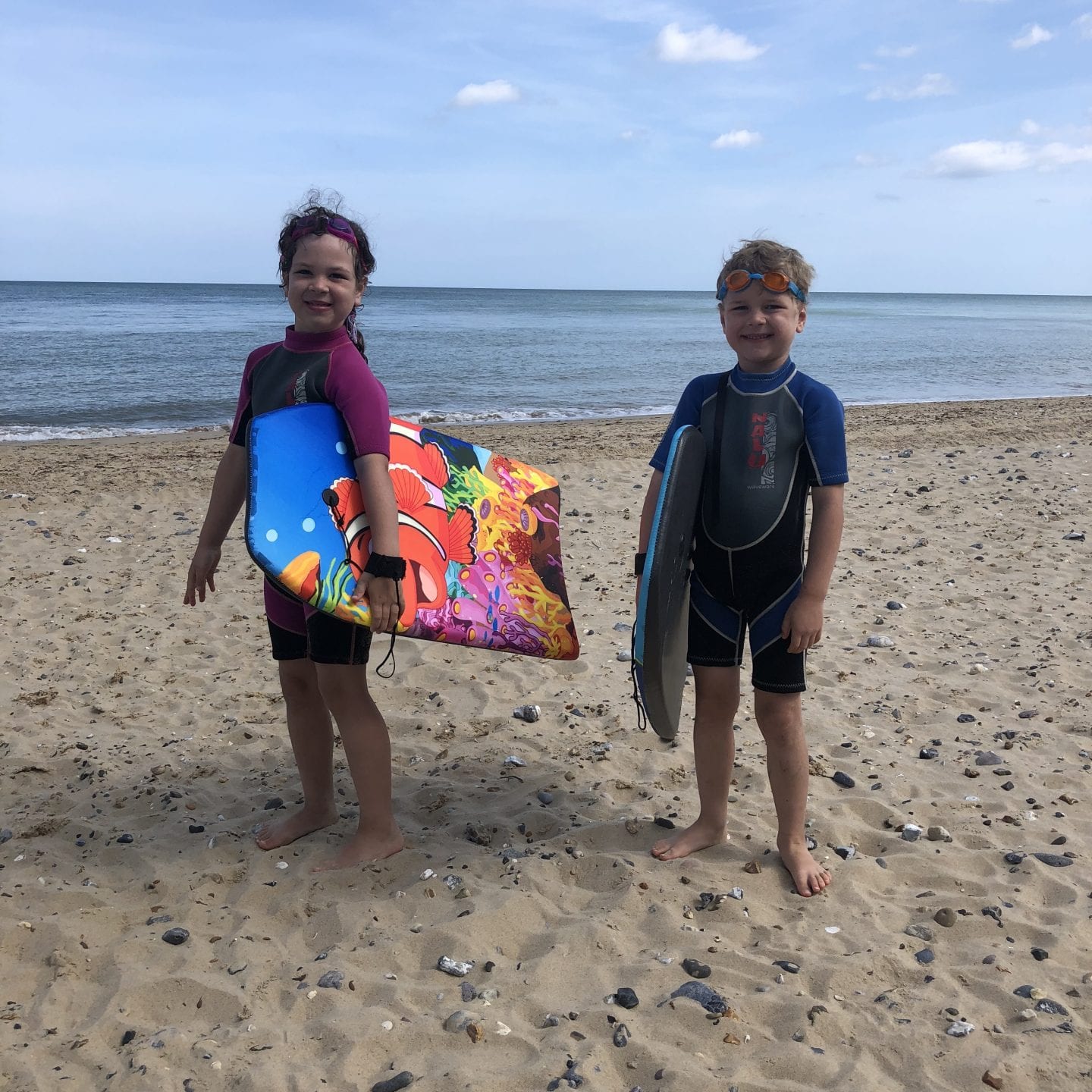 2 children holding body boards on a beach