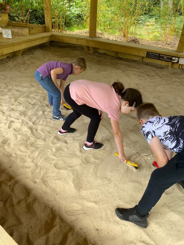 3 children in a sand pit looking for fossils