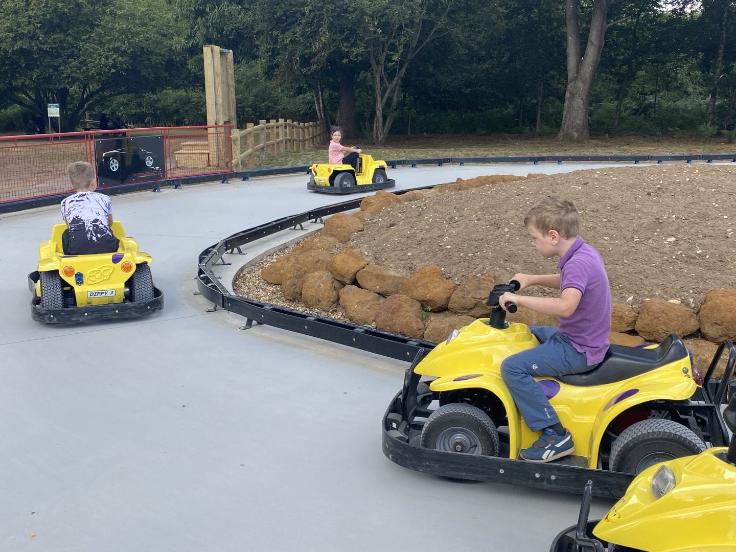 3 children riding on small electric cars around a track
