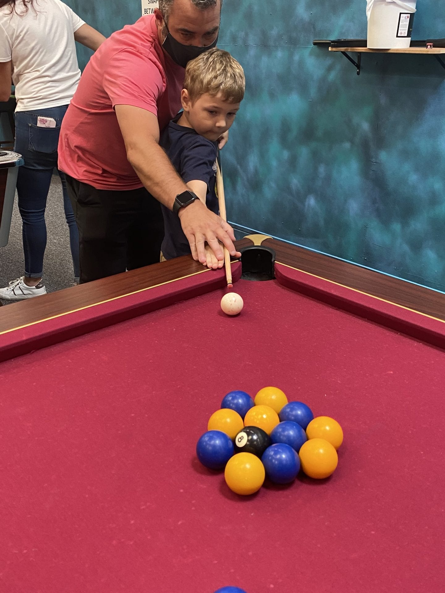 A dad teaching his son how to hit the que ball in pool