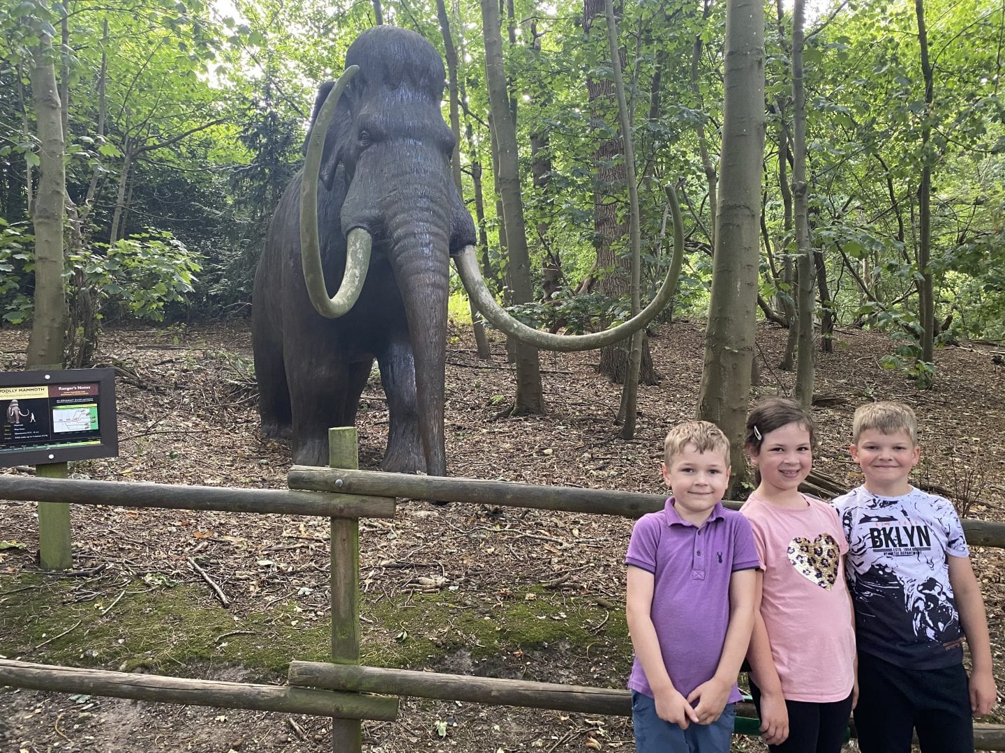 3 children standing in front of a staue of a wooly mammoth