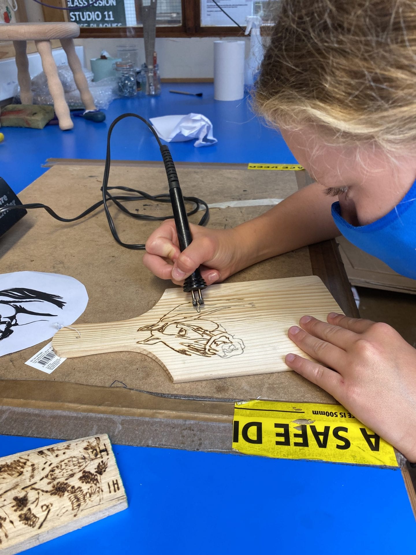 A young girl using pyrography to draw a horse on a small wooden chopping board