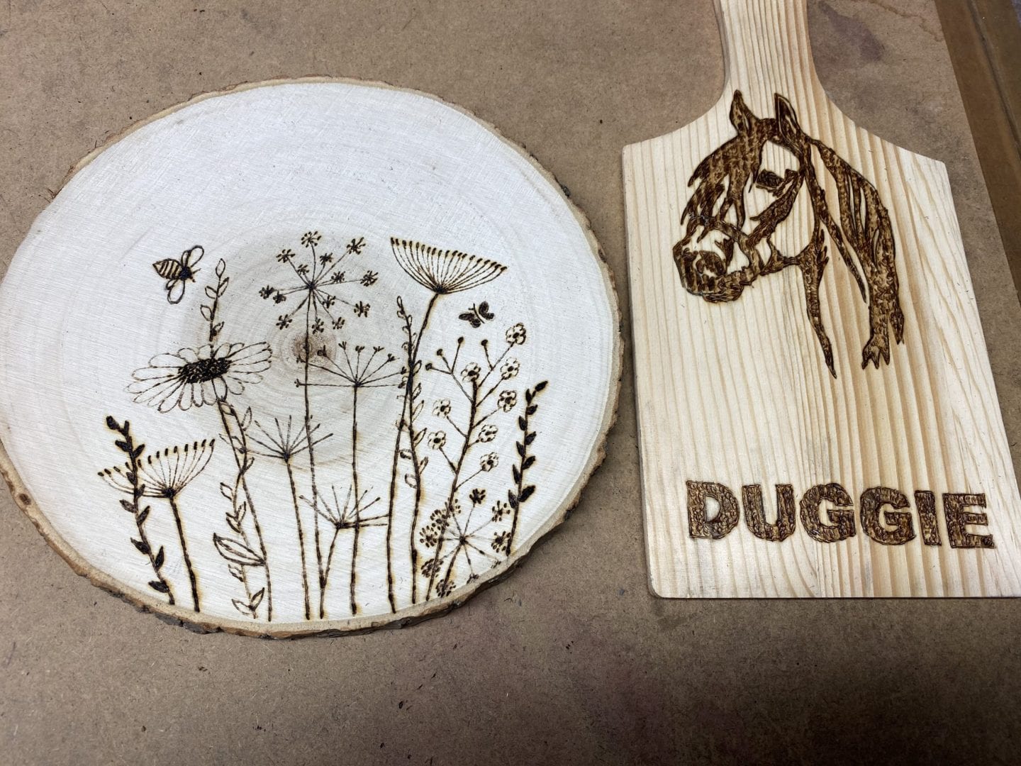 two pyrography projects- one wood slice with a floral pattern, the other a small chopping board with a horse