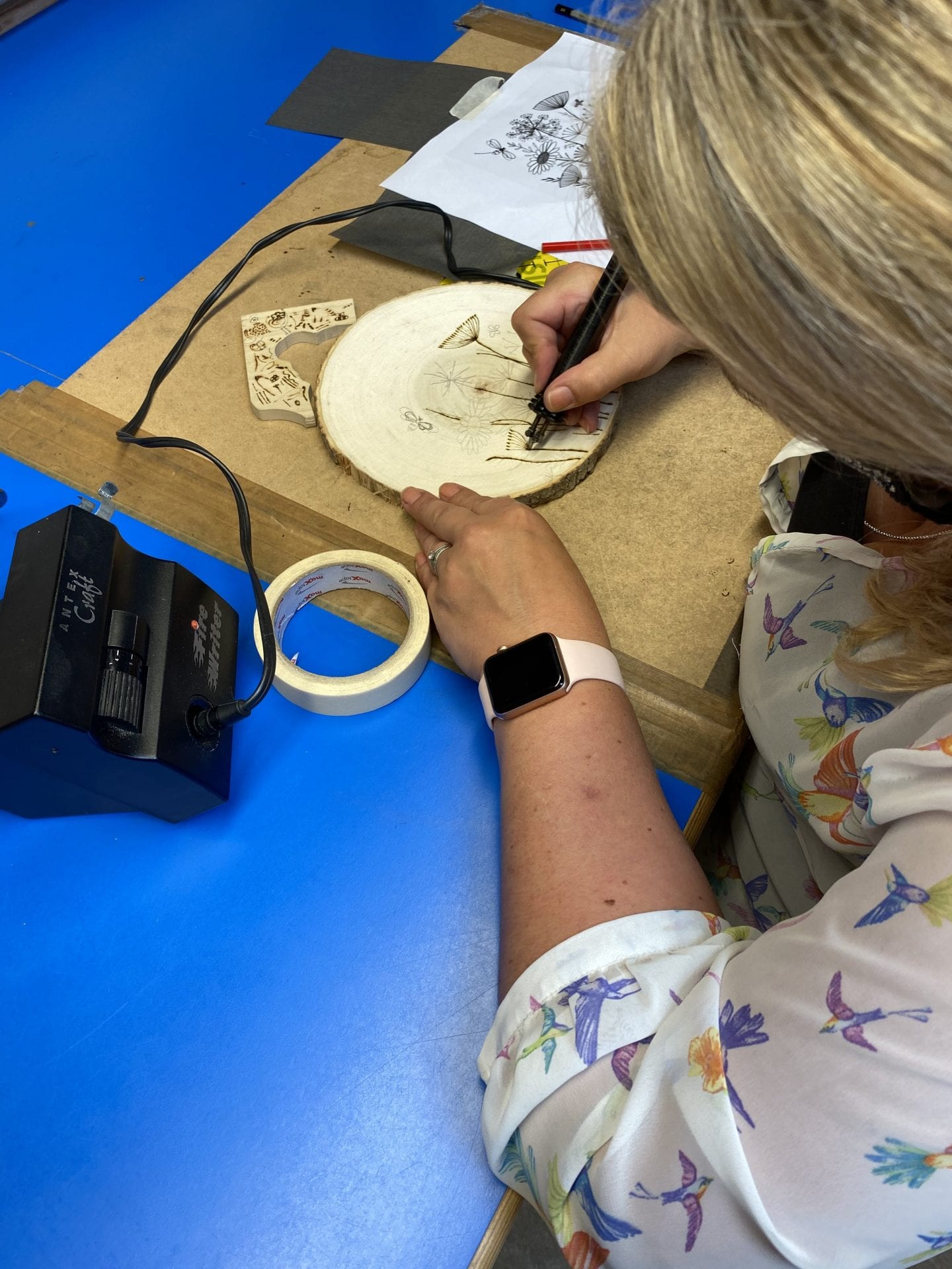 A wome using a pyrography pen to burn a design into a wood slice