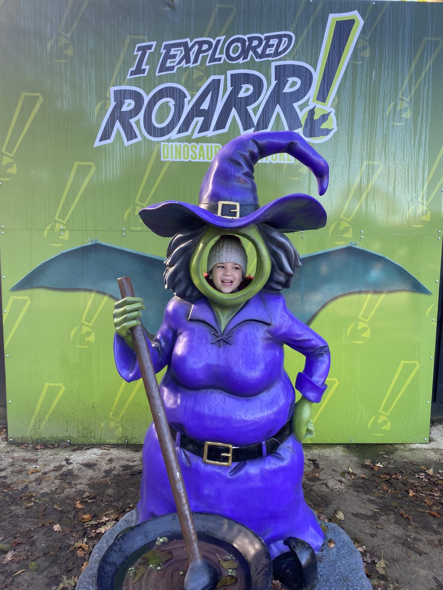 A young girl standing behind a statue of a witch