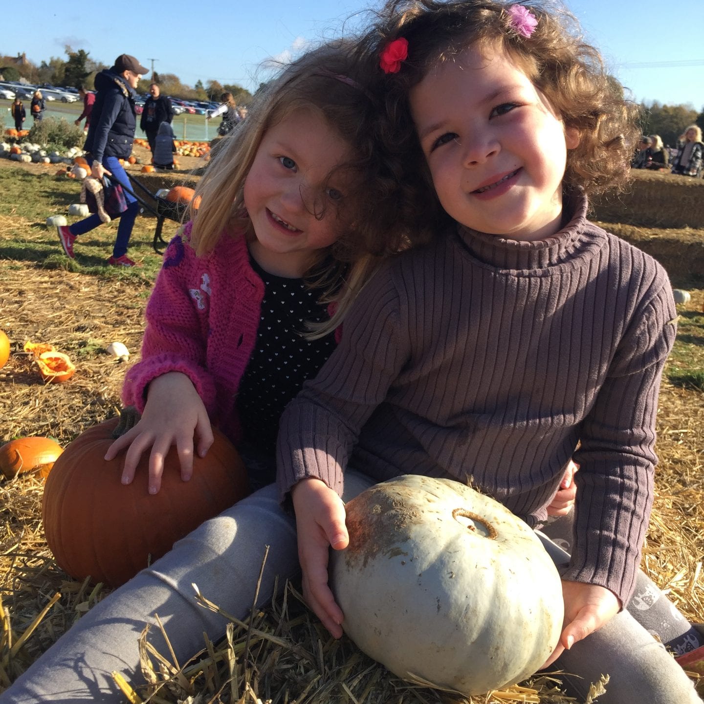 2 young girls sitting on a straw bale with their pumpkins
