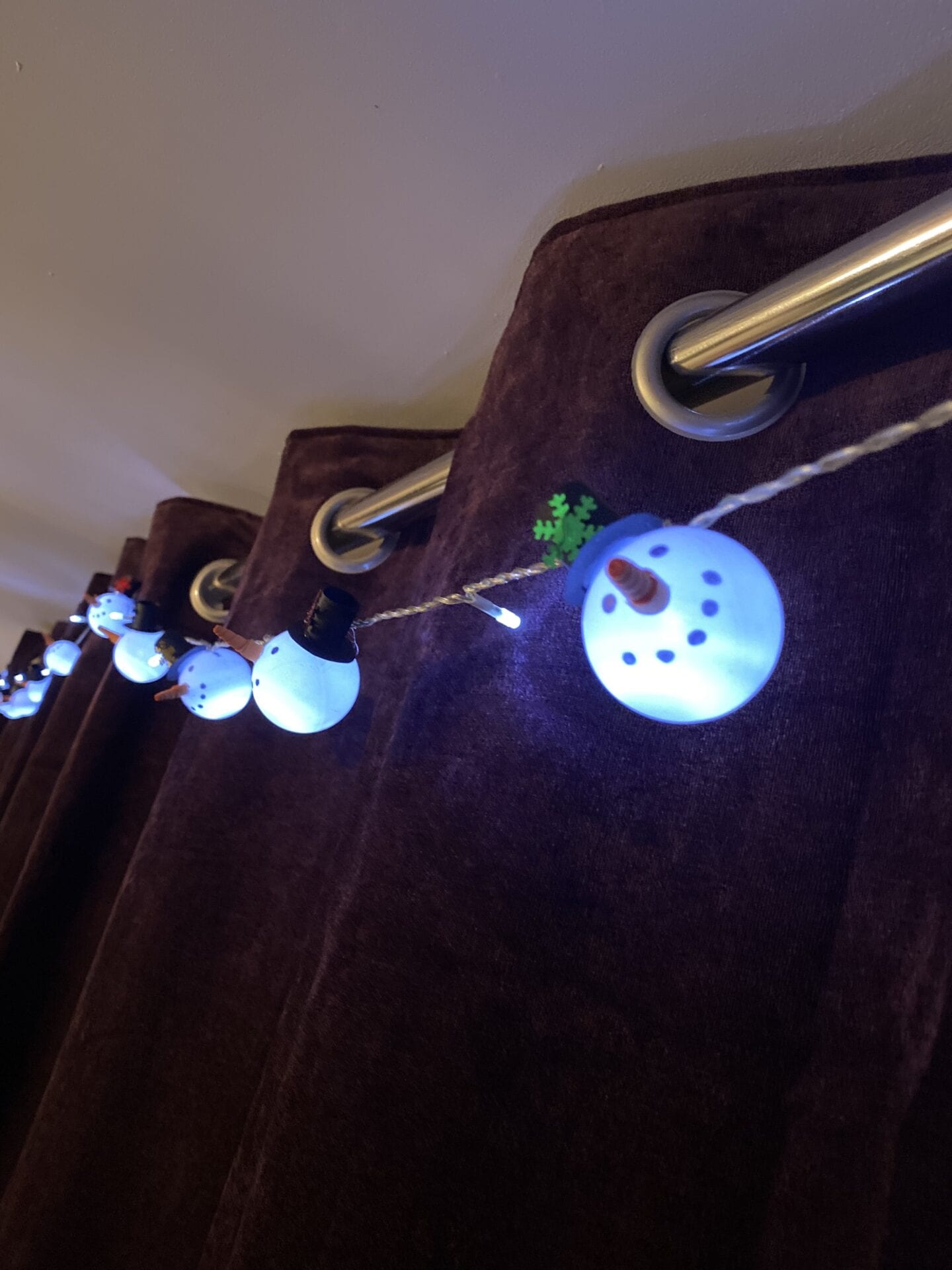 A string of pin pong snowman lights hung up in front of a dark puruple curtain