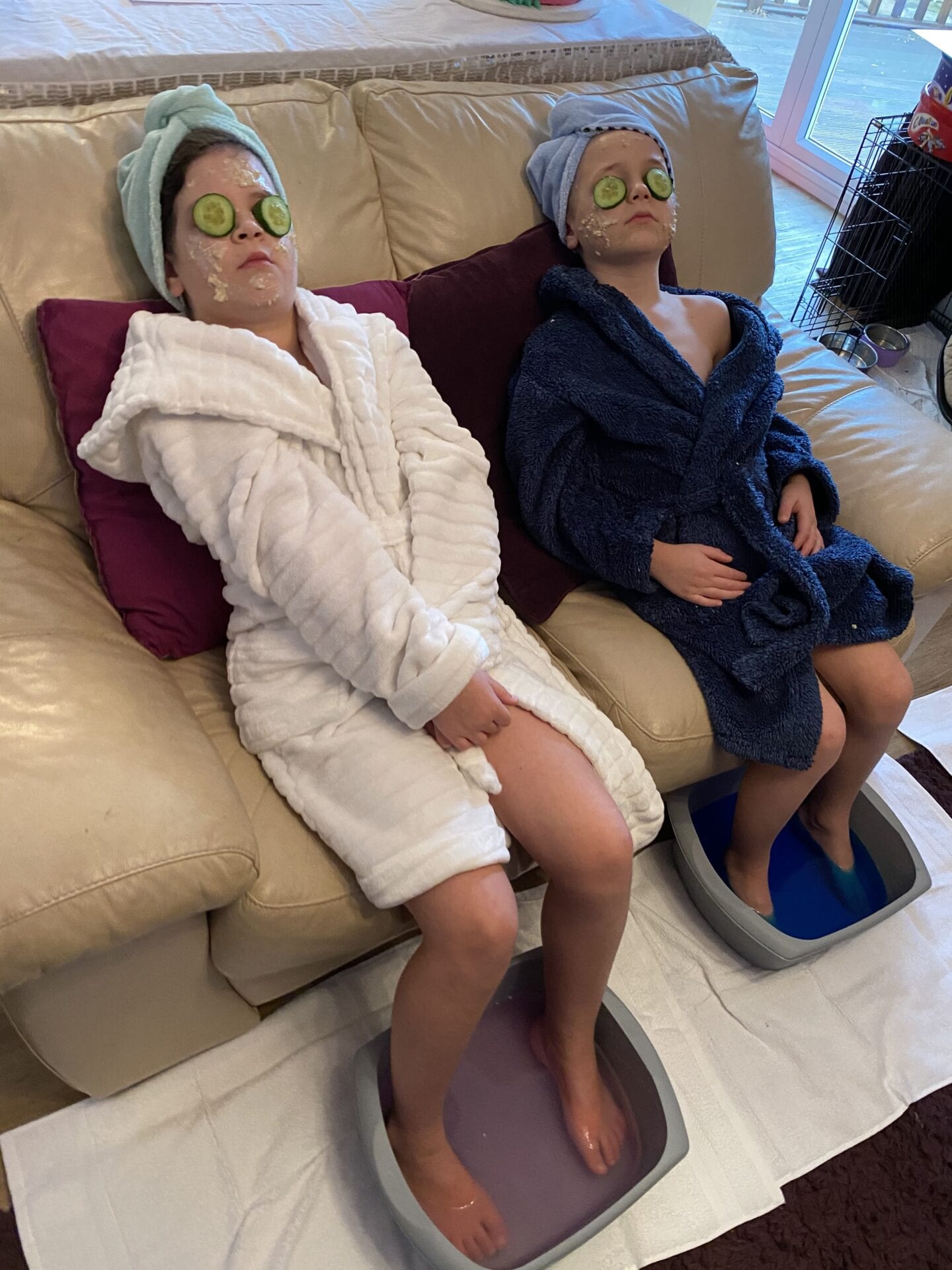 2 children in dressing gowns with face masks on, relaxing with cucumber on their eyes.